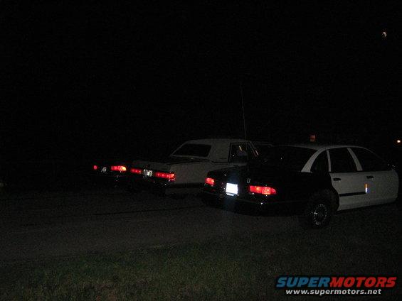 Rear view of a black and white police car and two sedans at night