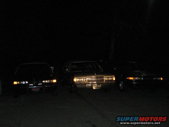 Three sedans parked at night, one is a 1988 Mercury Grand Marquis