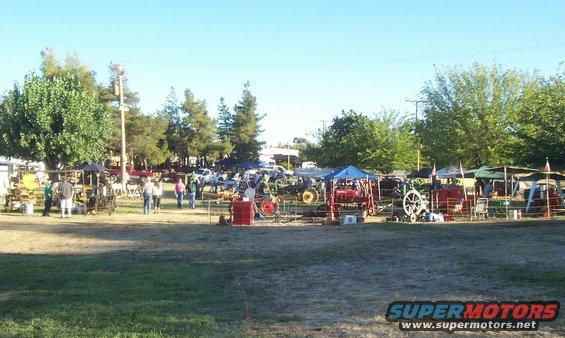 Outdoor market scene with multiple tractors, tents, and people browsing