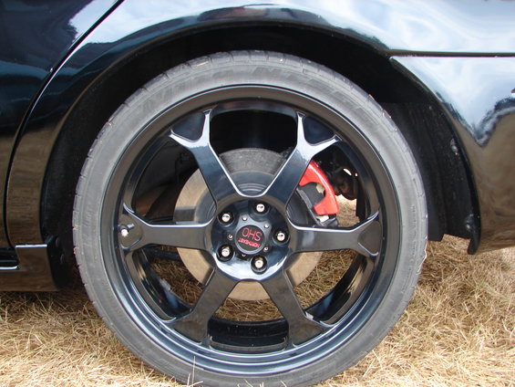 Black car wheel with red brake caliper and 'OHS' center cap