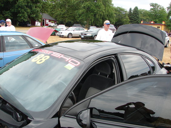 Black sedan with "BURNOUT SHO 88" decal on windshield, parked at an outdoor event