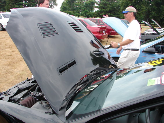 Black car hood open, showing engine bay. People and other cars in background