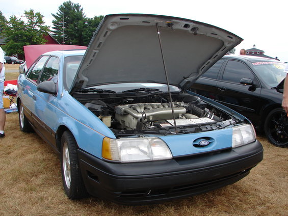 Light blue sedan, hood open, showing V6 engine. Black trim, front view