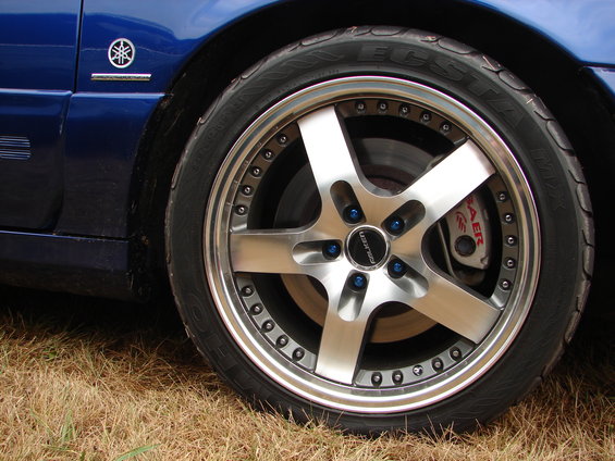 Close-up of a custom five-spoke alloy wheel with blue lug nuts and a red brake caliper. Falken tire visible