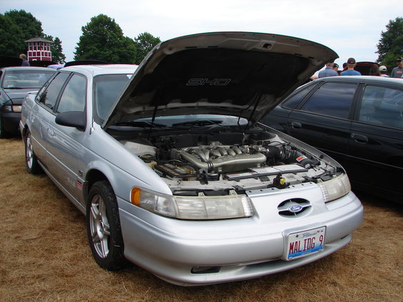 Silver 1993 Ford Taurus SHO with hood open, showing the engine. Another car is parked next to it