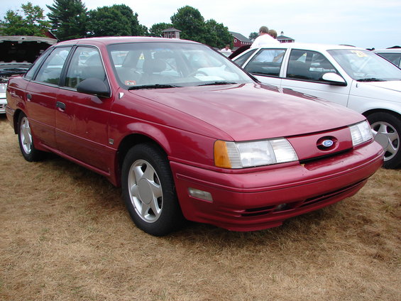 Red 1992 Ford Taurus sedan parked on dry grass, front 3/4 view