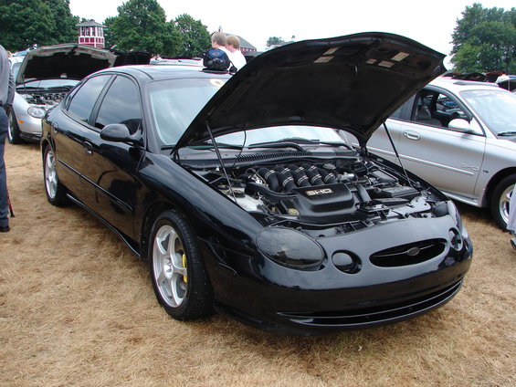 Black Ford Taurus with hood open, showing engine. Yellow brake calipers visible