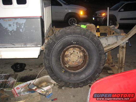 Truck chassis with a large tire, showing rust and wear. A beer bottle rests on the frame