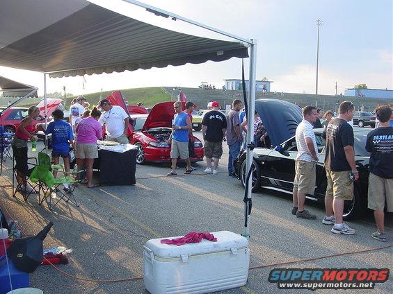 People gathered around cars at an outdoor event, some with hoods open