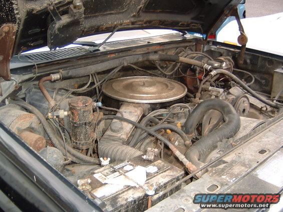 Engine bay of an older truck, showing the engine, battery, and various hoses and components