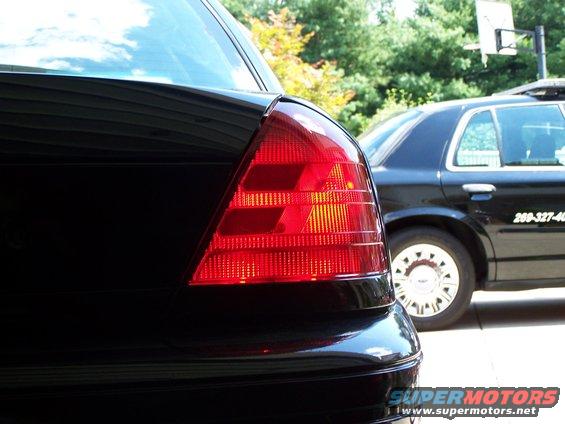 Black car's rear tail light, with a black police car visible behind it