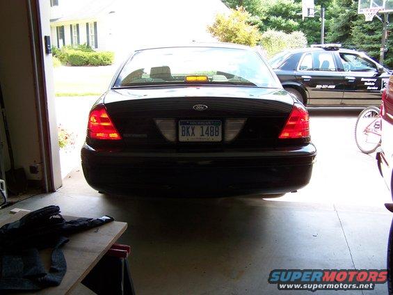 Rear view of a black 2003 Ford Crown Victoria parked in a garage, with another black vehicle visible outside