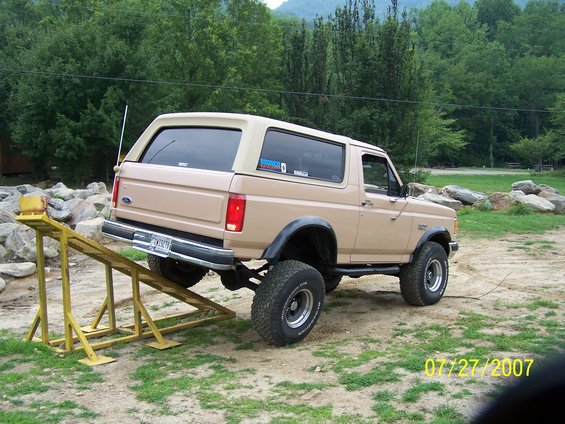 Tan Ford Bronco with a lift kit on a yellow ramp, rear view