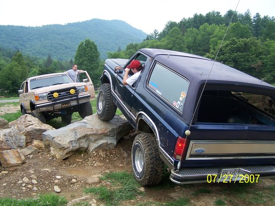 Dark blue Ford Bronco climbing rocks, with a tan Ford Bronco behind it
