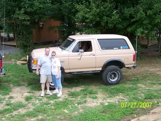 Tan Ford Bronco with a man and woman standing in front, lifted suspension, aftermarket bumper