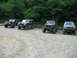 1992 Ford Mustang - A collection of four off-road vehicles are parked in a gravel lot surrounded by dense foliage.
