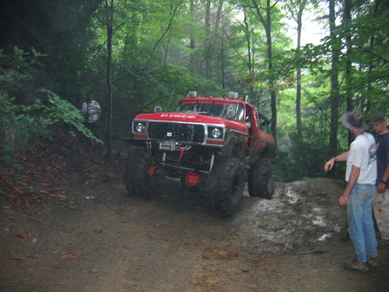 Red off-road truck with large tires on a muddy trail, front view