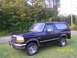 1993 Ford Bronco - A dark blue 1993 Ford Bronco is parked on a grassy area with trees behind it.