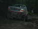1992 Ford Mustang - A lifted Ford Bronco navigates a challenging off-road course in a wooded area.