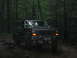 1992 Ford Mustang - A dark colored Ford Bronco navigates a rocky, wooded trail.