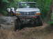 1992 Ford Mustang - A lifted Ford Bronco navigates a challenging off-road course with two people watching.