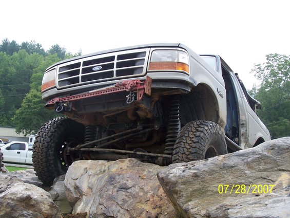Modified Ford truck with large tires on rocks, front grille visible