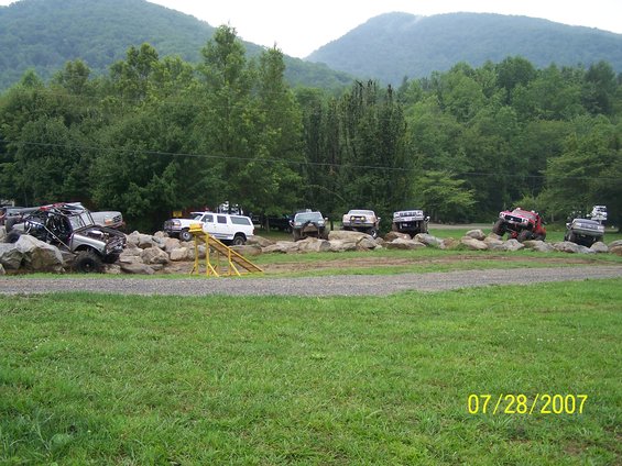 Several off-road vehicles are positioned on large rocks in a wooded area