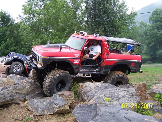 Red 1979 Ford F-150 off-roading over rocks, driver visible