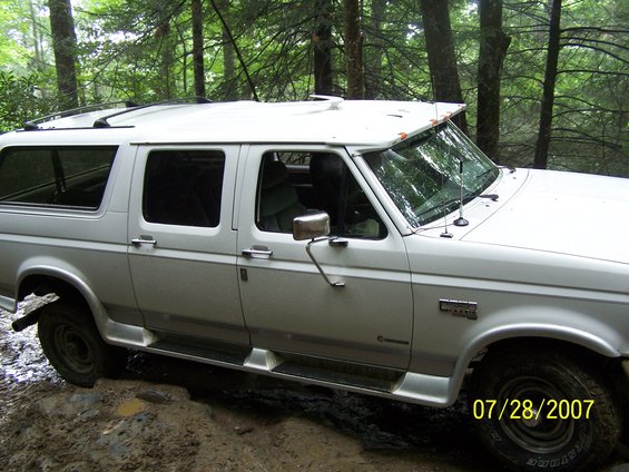 White SUV with roof rack driving on a muddy trail in the woods