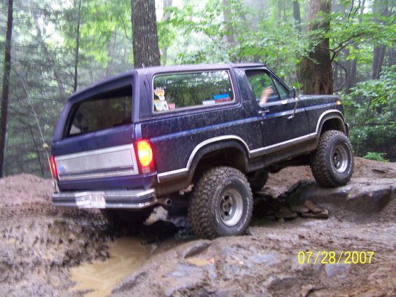 Blue Ford Bronco climbing over rocks and mud on a trail