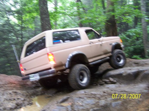 Tan SUV with a removable hardtop navigating a rocky, muddy off-road trail