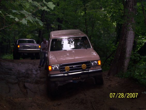 Tan van with smiley face lights on grille, driving off-road