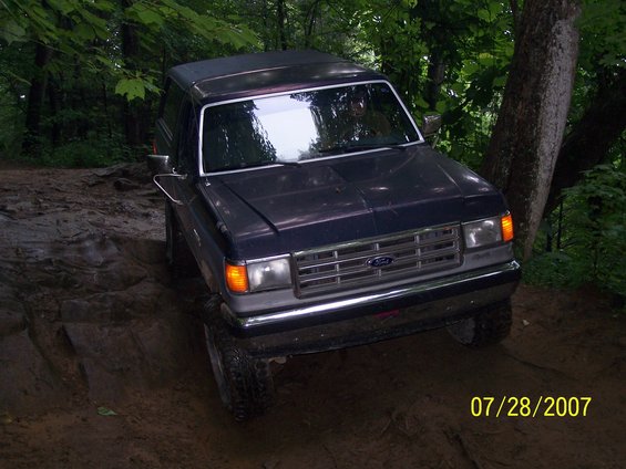 Dark blue Ford Bronco climbing a muddy hill in a wooded area. Date stamp reads 07/28/2007