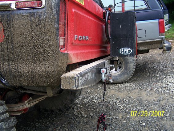 Mud-covered red Ford pickup truck rear bumper with tow hitch and a silver truck behind it
