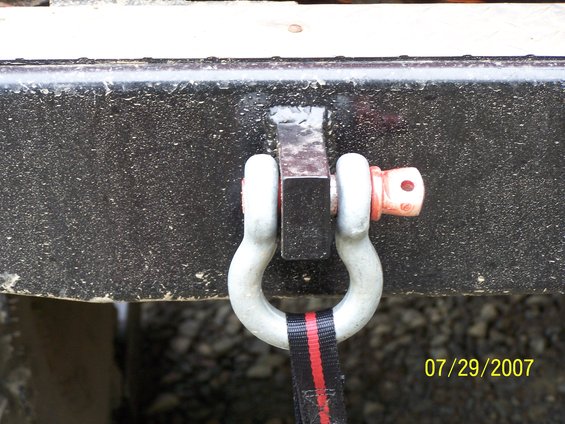 Close-up of a tow shackle with a red and black strap attached to a dark, textured vehicle frame