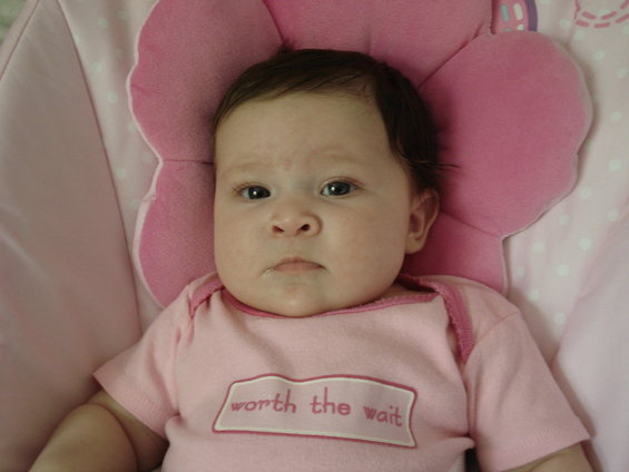 Baby wearing a pink onesie with the words "worth the wait" on it, lying on a pink floral pillow