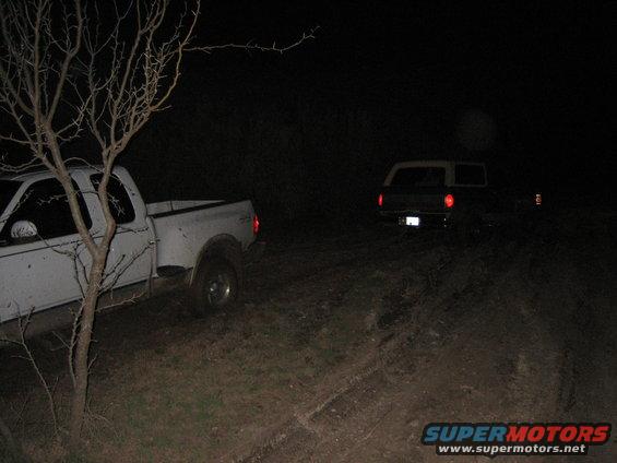 White pickup truck and a dark SUV parked on a dirt road at night