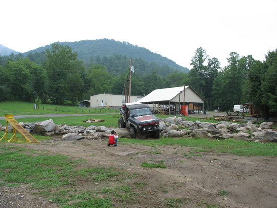 off-road vehicle driving over rocks, person on red toy nearby