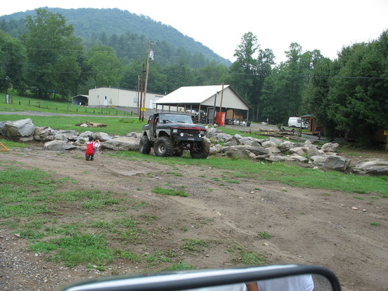 Modified off-road vehicle with large tires and lifted suspension, dark gray body with red accents on the grille, parked on a dirt path