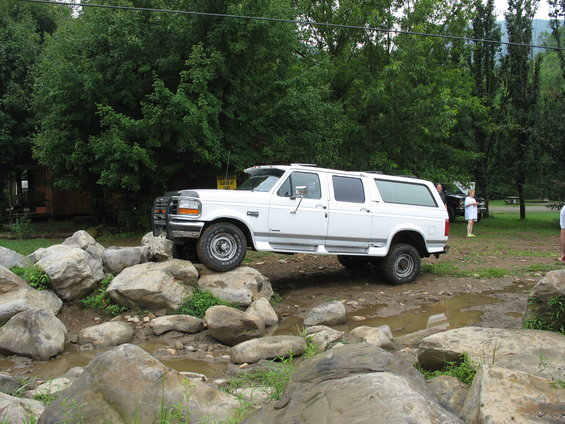 White extended cab pickup truck with a camper shell on rocks, 3/4 front view