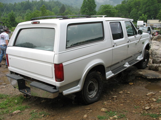 White SUV with camper shell on rocky terrain. Rear view