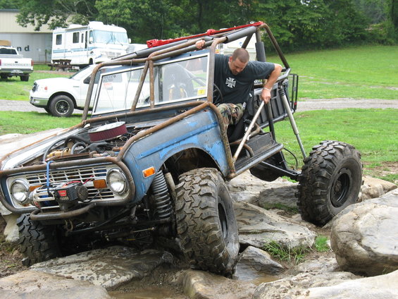 Custom buggy with roll cage going over rocks. A man is climbing into the driver's seat