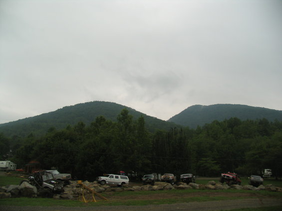 Several off-road vehicles parked on rocky terrain with trees and mountains in the background