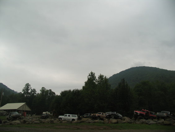 Several trucks and SUVs parked on rocks with trees and a hill in the background
