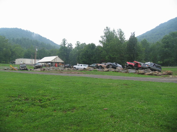 Several off-road vehicles are parked on large rocks in front of a building and trees