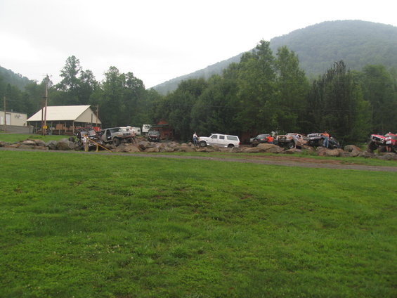Off-road vehicles parked on rocks with a building and trees in the background