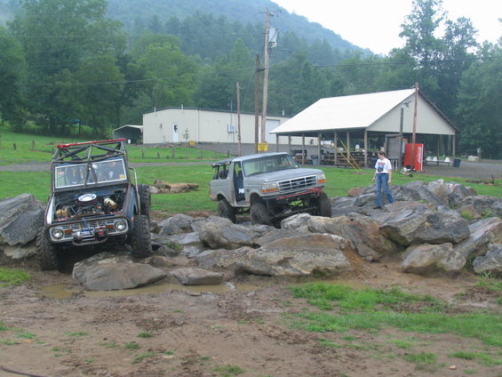 Silver Ford Bronco off-roading over rocks, hood open. Another off-road vehicle in background