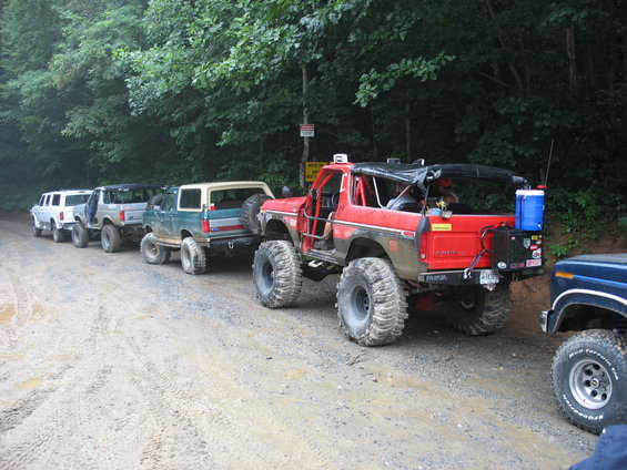Red off-road Bronco with large tires and roll cage, parked on a dirt road