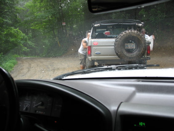 Silver SUV with spare tire on rear, seen from inside another vehicle on a dirt road