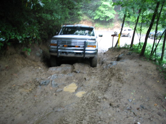 1995 Ford C-350 (Centurion Conversions) navigating a muddy, rocky trail with another vehicle visible in the background